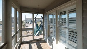 Eine überdachte Veranda mit einer Hängematte, großen Fenstern und Blick auf die Umgebung.