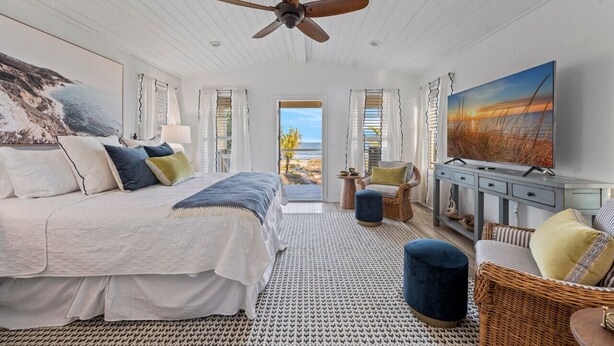 Une chambre avec un grand lit, un ventilateur de plafond, une vue sur la plage et un téléviseur.
