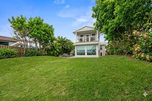 A two-story house with a large lawn, a patio, and a variety of plants and flowers.