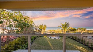 Un balcon avec vue sur la plage et l’océan au coucher du soleil.