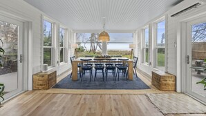 Un espace repas avec une table et des chaises en bois, de grandes fenêtres et une vue sur l’extérieur.