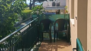 Un espace extérieur abrité, doté d’un sol carrelé, d’une rambarde en métal et de deux chaises en plastique.
