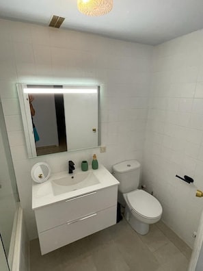 Une petite salle de bain propre, avec un lavabo blanc, un miroir et des toilettes.