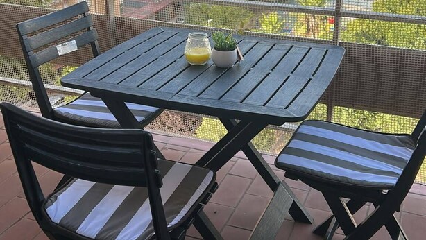 Ein Balkon im Freien mit Tisch, Stühlen, einem kleinen Topfpflanzen und einem Glas Orangensaft.