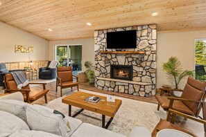 A cozy living room with a stone fireplace, comfortable seating, and a flat-screen TV mounted above it. - Mill Creek Rd Lakehouse (Ronald)