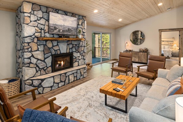 A cozy living room with a stone fireplace, comfortable seating, and a view to the outdoors.