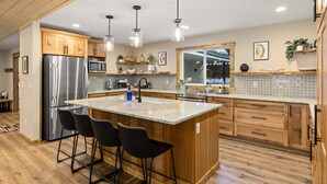 A modern kitchen with wooden cabinets, stainless steel appliances, and a large island with bar stools. - Mill Creek Rd Lakehouse (Ronald)