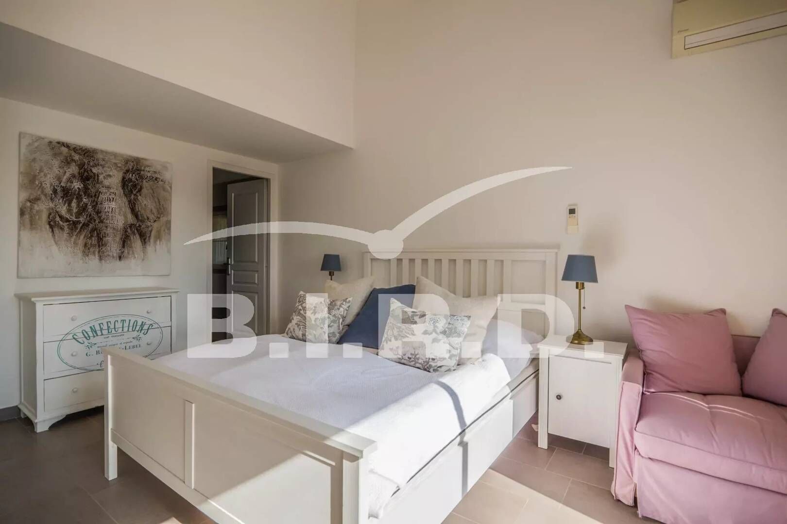 Ein Schlafzimmer mit einem Bett, Nachttischen, einem Beistelltisch, einem rosa Sofa und einer Wand mit einer Dekoration.