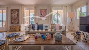 A living room with a sofa, a coffee table with decorative items, a television, and a view of the outdoors. - Provençal villa with sea view (STE MAXIME)