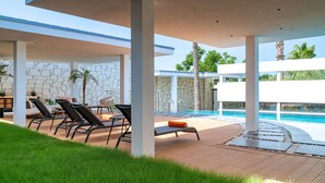 A modern outdoor pool area with lounge chairs, a stone wall, and a clear view of the pool. - Royal Teos Thermal Resort Clinic & Spa - Halal Hotel (Seferihisar)