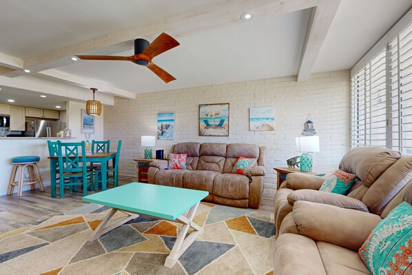 A spacious living room with a brown leather sofa, teal coffee table, and a ceiling fan. - Shared Pool, Charcoal Grill, Golf Cart access (Port Aransas)
