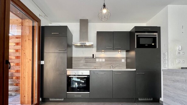 Une cuisine moderne dotée d’appareils électroménagers intégrés, d’une grande fenêtre et d’une porte en bois.