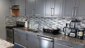 A modern kitchen with grey cabinets, a stainless steel dishwasher, a coffee maker, and a blender. - 3 minutes to the lake for.  lower suite with separate entrance.  (chestermere)