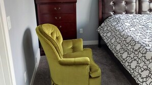 A bedroom with a bed, a wooden dresser, and a yellow armchair. - 3 minutes to the lake for.  lower suite with separate entrance.  (chestermere)