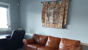 A living room with a brown leather sofa, patterned rug, and a tapestry on the wall. - 3 minutes to the lake for.  lower suite with separate entrance.  (chestermere)