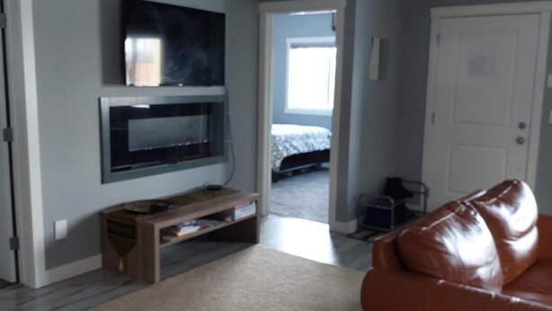 A living room with a flat-screen TV, a brown leather sofa, and a wooden entertainment unit. - 3 minutes to the lake for.  lower suite with separate entrance.  (chestermere)