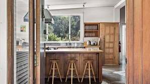 A kitchen with a large window, wooden stools, and a wooden cabinet. - Wisteria Vines Estate—Rustic Elegance by the Coast (Wilyabrup)