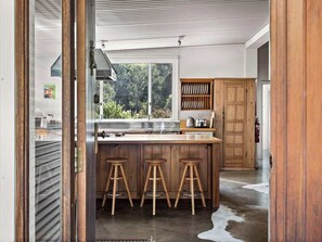 A kitchen with a large window, wooden stools, and a wooden cabinet. - Wisteria Vines Estate—Rustic Elegance by the Coast (Wilyabrup)