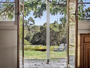 A view through a glass door with a garden, a lawn, and a chair outside. - Wisteria Vines Estate—Rustic Elegance by the Coast (Wilyabrup)