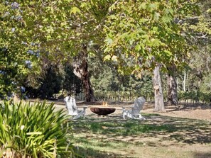 A fire pit surrounded by white chairs in a park-like setting with trees. - Wisteria Vines Estate—Rustic Elegance by the Coast (Wilyabrup)