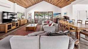 A spacious living area with a high ceiling, a large flat-screen TV, a dining table, and comfortable seating. - Wisteria Vines Estate—Rustic Elegance by the Coast (Wilyabrup)