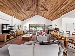 A spacious living area with a high ceiling, a large flat-screen TV, a dining table, and comfortable seating. - Wisteria Vines Estate—Rustic Elegance by the Coast (Wilyabrup)