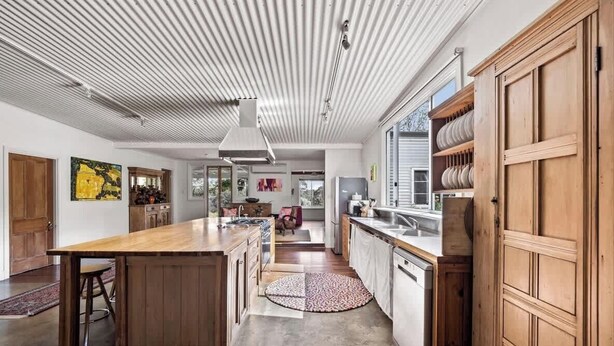 A modern kitchen with a central island, wooden cabinets, and a view to the living area. - Wisteria Vines Estate—Rustic Elegance by the Coast (Wilyabrup)