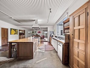 A modern kitchen with a central island, wooden cabinets, and a view to the living area. - Wisteria Vines Estate—Rustic Elegance by the Coast (Wilyabrup)