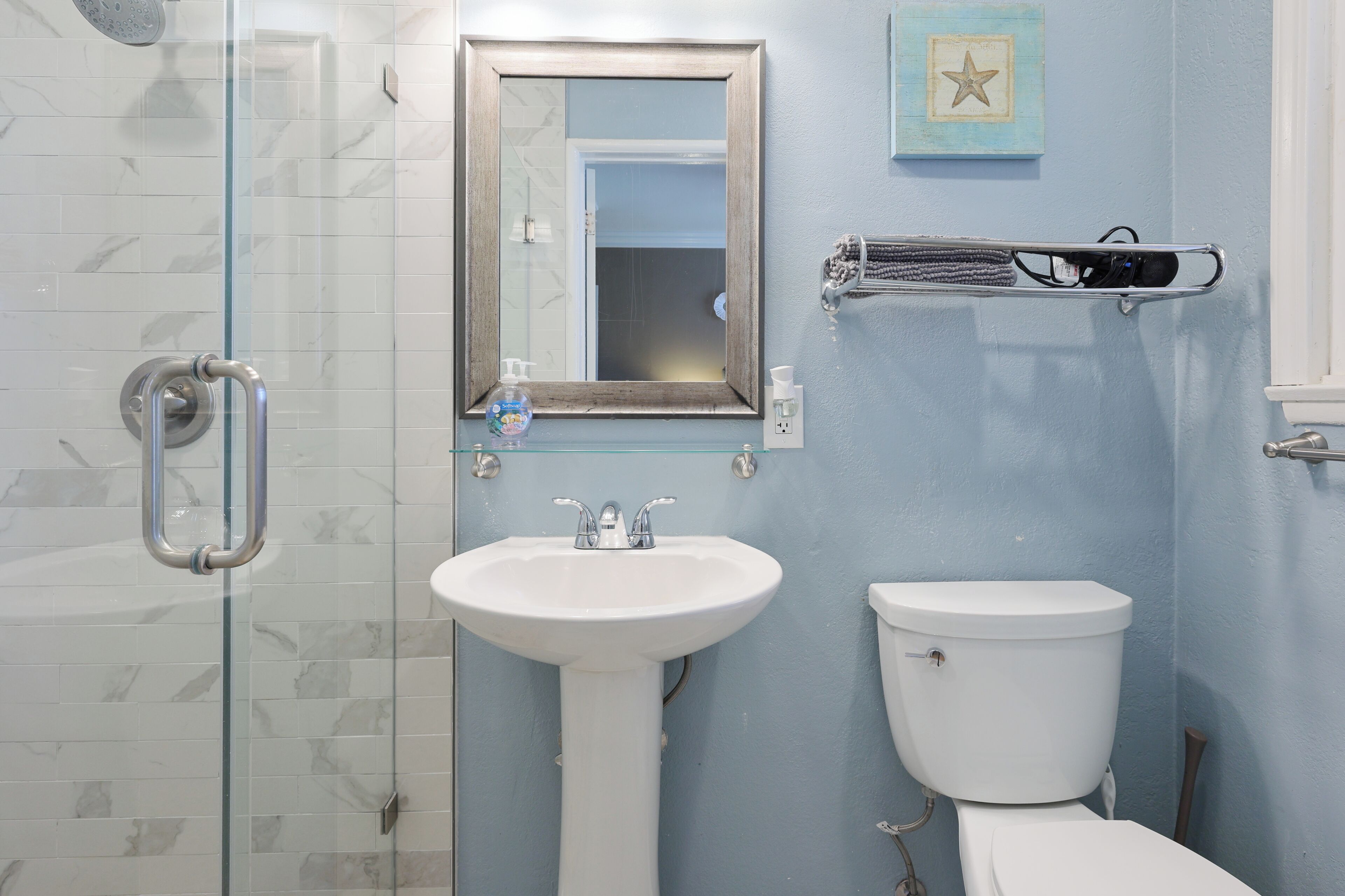 Un baño con cabina de ducha de vidrio, un lavamanos blanco y un inodoro.