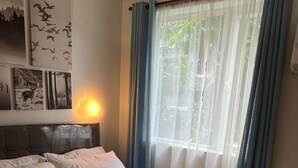 A neatly made bed with white linens, a headboard with a light-colored fabric, and a window with blue curtains.