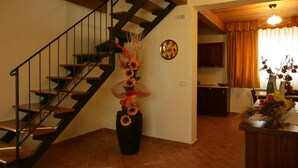Eine Treppe mit Holzboden und schwarzen Geländern, ein Blumentopf mit Sonnenblumen, ein Küchenbereich mit Holzausbau und ein Esstisch mit Blumenvase.