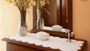 Eine Holzkommode mit zwei gestreiften Vasen voller Blumen, einer weißen Spitzklängetuch und einem Spiegel, der einen Schrank und eine Wand mit gerahmten Bildern reflektiert.
