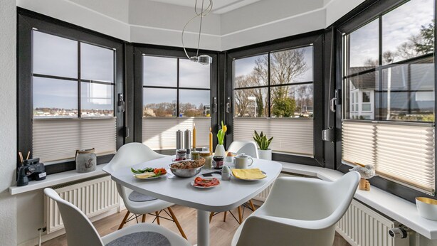 A corner dining area with a table set for two, a view of the outdoors, and a window with blinds.