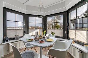 A corner dining area with a table set for two, a view of the outdoors, and a window with blinds.