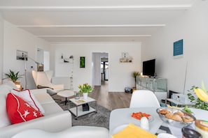 A modern living room with a sofa, armchair, coffee table, and a dining area with a table set for a meal.