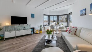 A modern living room with a flat-screen TV, a glass cabinet, a white sofa, and a dining area with a table and chairs.