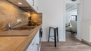 A modern kitchen with a wooden countertop, stainless steel sink, and a clock on the wall.