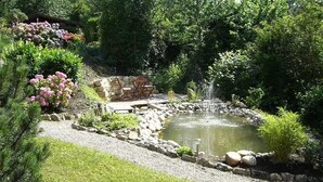 Ein Garten mit Teich, Sitzgelegenheit und umgebender Bepflanzung.