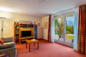 Een woonkamer met een televisie, een boekenkast en een schuifdeur naar een buitenruimte.