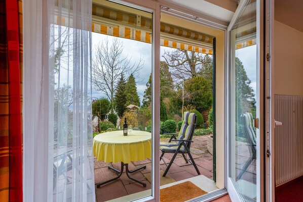 Een kamer met een schuifdeur die uitkomt op een terras buiten, met een tafel en stoelen.