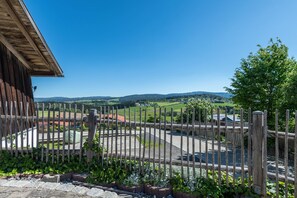 Une clôture en bois, une zone pavée et, au loin, une vue sur des champs et des collines verdoyants.