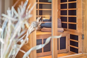 Een houten sauna met een bank en handdoeken, een houten deur en uitzicht op een kamer met een bed.