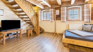 Eine Holztreppe, ein Bett, ein Fernseher und zwei Fenster mit Vorhängen.
