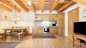 Ein Holzinterieur mit einem Esstisch, Bänken, einer Küche mit Holzausbau, einem Fernseher und einer Decke mit freiliegenden Balken.