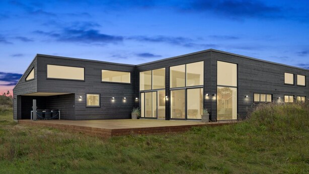 A modern two-story house with large windows, a flat roof, and a wooden deck.