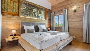 A wooden-paneled room with a bed, a nightstand, a wall-mounted lamp, and a window with curtains. - Chalet 'Bergchalet 3' with Private Pool, Private Terrace and Wi-Fi (Freyung)