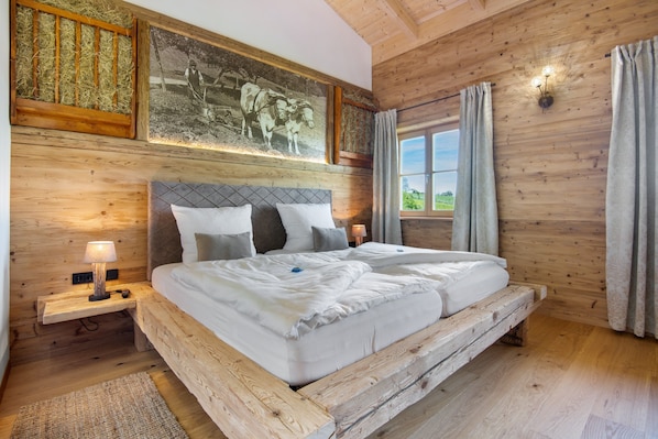A wooden-paneled room with a bed, a nightstand, a wall-mounted lamp, and a window with curtains.