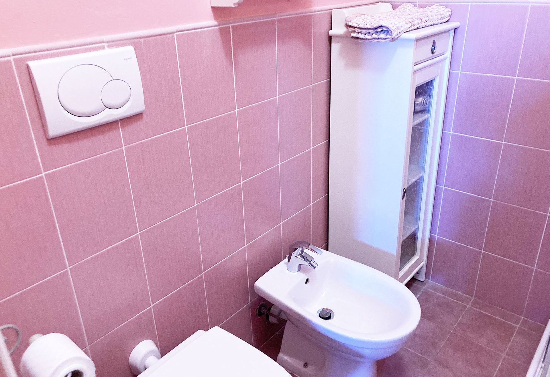 Un baño con azulejos rosas, un inodoro blanco, un bidé y un perchero para toallas.
