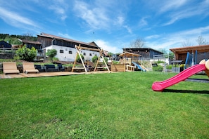 A playground with a slide, swings, and a climbing structure in a grassy area with houses in the background.