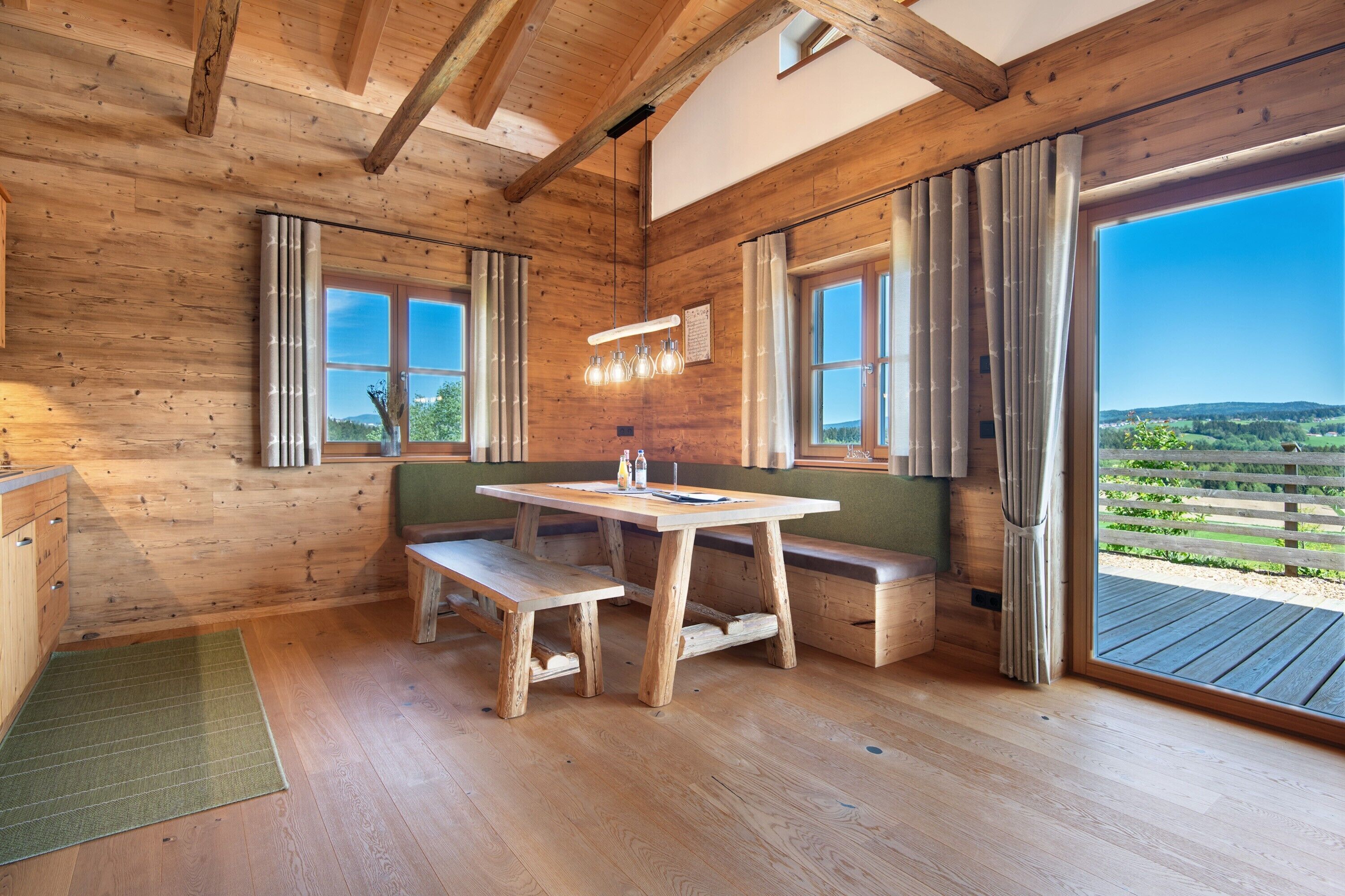 A wooden interior with a wooden table, bench, and large windows offering a view of the outdoors.